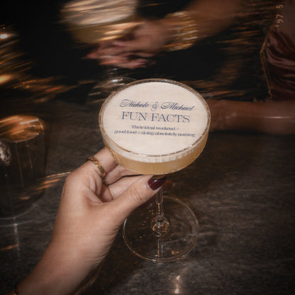 Cocktail glass with a label titled 'Fun Facts' held by a hand on a dark surface.