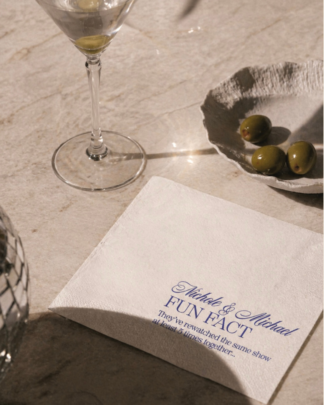 Napkin with text on a table with a glass and olives